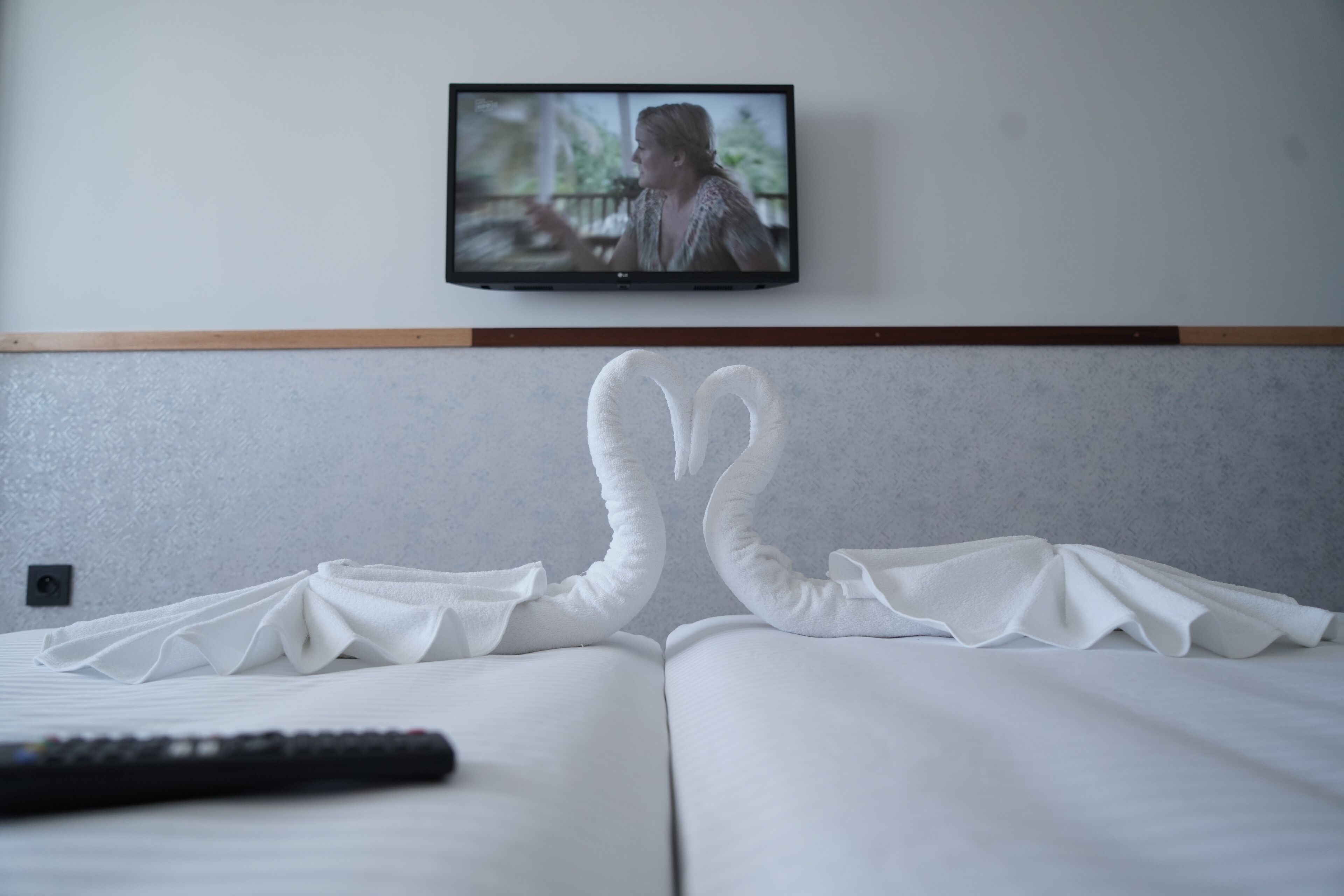 A hotel room with a bed, a remote control, and a television mounted on the wall.