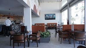 A modern cafe with marble counters, brown leather chairs, and a large TV screen. - Hôtel Seashell (Oualidia)