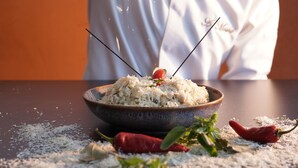 A bowl of food with a red chili pepper and a sprig of green herb on top, surrounded by scattered spices and a red chili pepper on a table. - Hôtel Seashell (Oualidia)