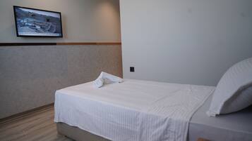 A neatly made bed with a rolled towel, a television mounted on the wall, and a wooden floor.
