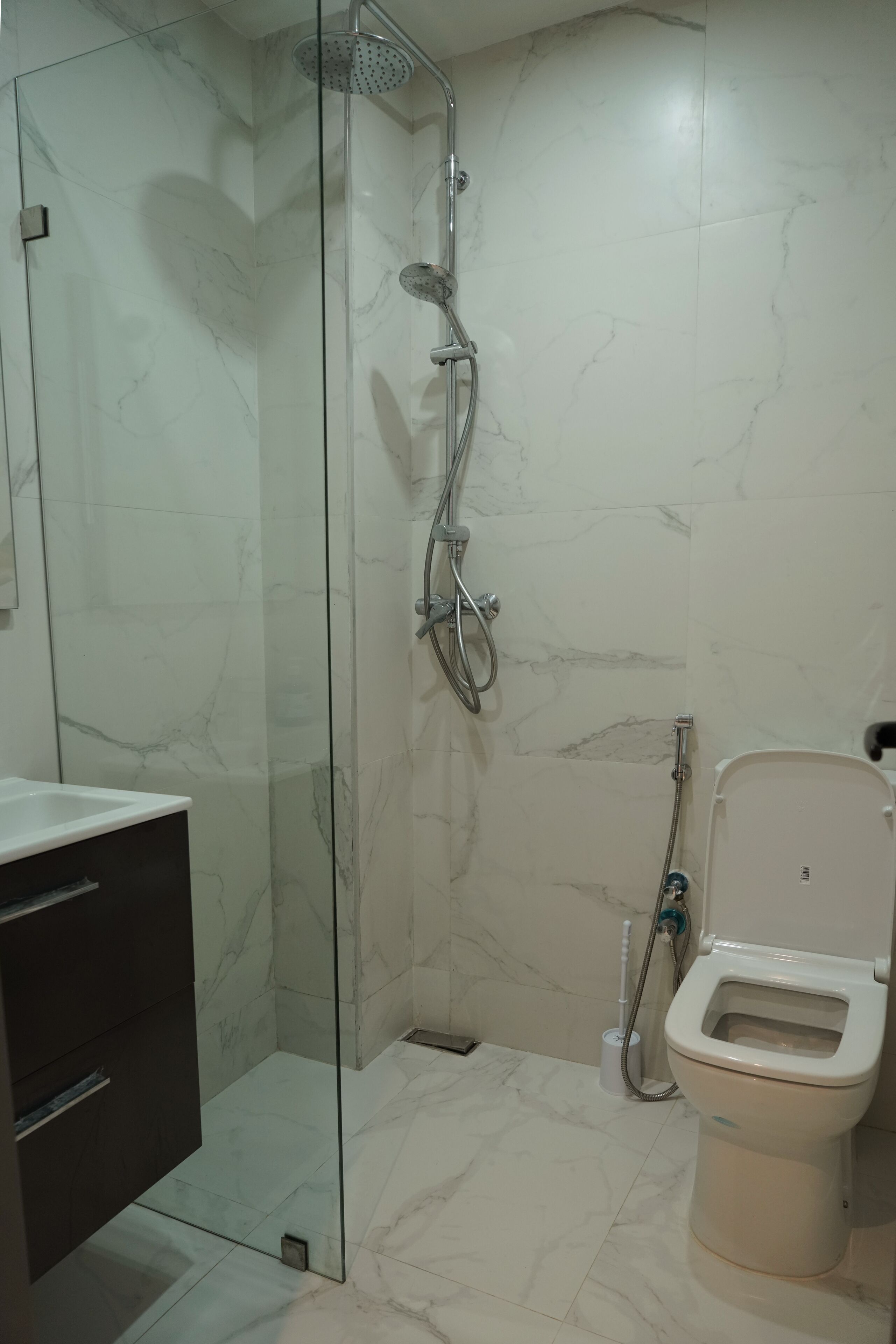 A bathroom with a glass-enclosed shower, a toilet, and a dark-colored cabinet.