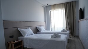 A hotel room with two beds, a TV mounted on the wall, and a window with curtains. - Hôtel Seashell (Oualidia)