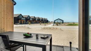 Ein Gebäude direkt am Strand mit Holzfassade, einem Essbereich mit Tisch und Stühlen sowie Blick auf Strand und Meer.