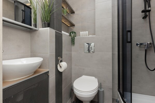 A modern bathroom with a large white sink, toilet, and shower area.
