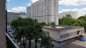 A high-rise building with a grid-like facade, surrounded by trees and other buildings.