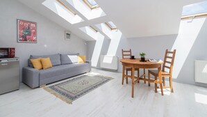 A modern loft apartment with skylights, a grey sofa, wooden dining table, and a small kitchen area. - Modern Studio in the heart of Kazimierz | Close to Attractions (Kraków)