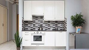 A compact kitchen with white cabinets, a black and white tiled backsplash, a built-in oven, and a small countertop. There is a ceiling fan, a potted plant, and a grey sofa in the room. - Modern Studio in the heart of Kazimierz | Close to Attractions (Kraków)
