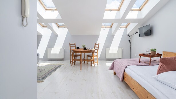 A modern loft bedroom with skylights, a wooden bed, a small table with a plant, and a TV mounted on the wall. - Modern Studio in the heart of Kazimierz | Close to Attractions (Kraków)