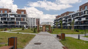 Un complejo residencial moderno con un camino central que conduce a un arco de madera, rodeado de vegetación y senderos pavimentados.