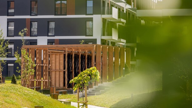 Un edificio moderno de varios pisos con balcones y una estructura de madera al frente.