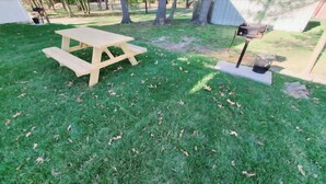 A wooden picnic table in a grassy yard with a barbecue grill and a trash can in the background. - Private Studio Apartment In Lewes (Lewes)