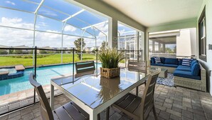 A covered patio area with a glass table, chairs, a blue sofa, and a view of a swimming pool. - Spacious Davenport Villa, Sleeps 21, Pool & Fun (Davenport)