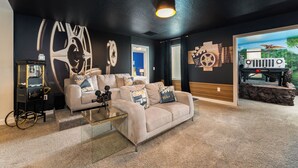 A living room with a beige sofa, a glass coffee table, and a wall with large mechanical wheel designs. - Spacious Davenport Villa, Sleeps 21, Pool & Fun (Davenport)