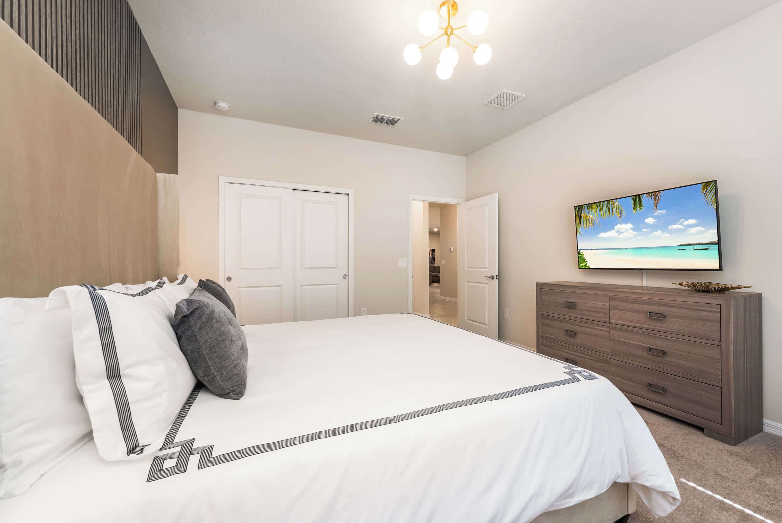 Un dormitorio con una cama, un aparador, un televisor y una puerta que da a otra habitación.