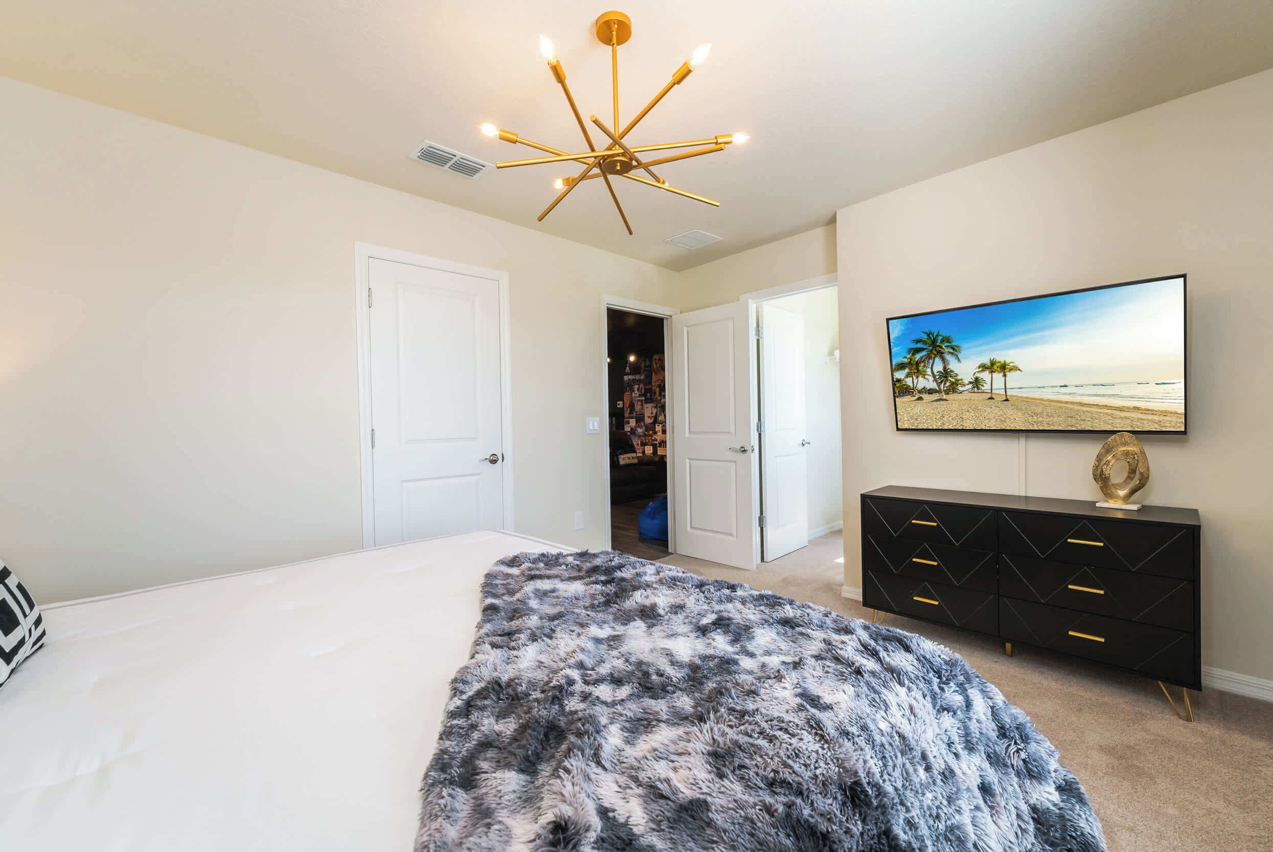 Een slaapkamer met een groot bed, een zacht tapijt, een zwarte dressoir met gouden handgrepen en een televisie aan de muur.