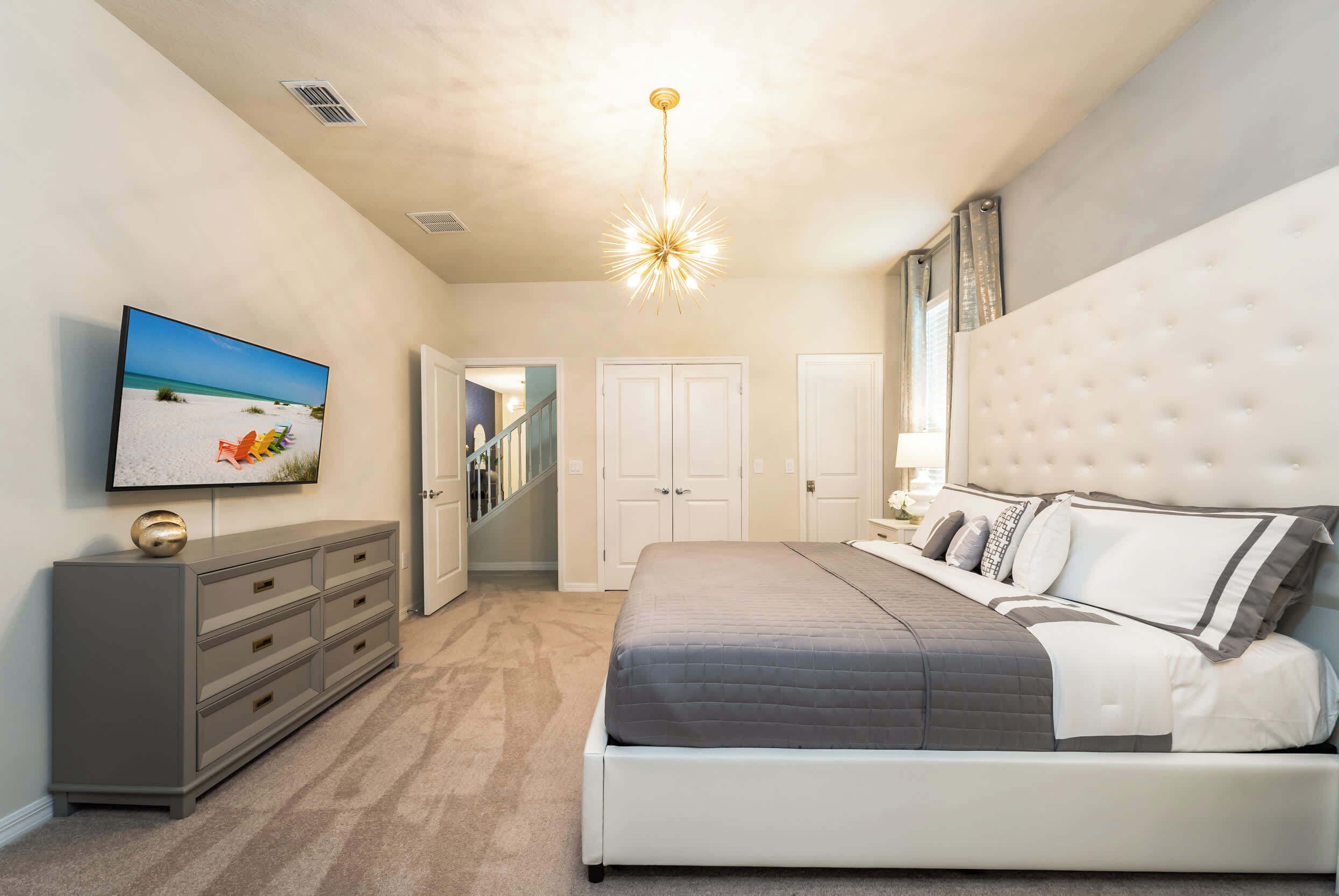A bedroom with a bed, a TV, a dresser, and a staircase.