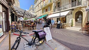A street with outdoor seating at cafes, a bicycle parked on the sidewalk, and a signboard. - LON5218 (Cannes)