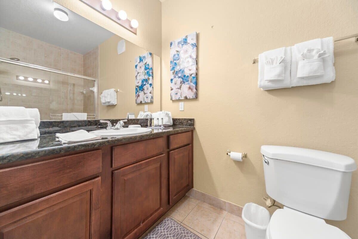 A bathroom with a marble countertop, wooden cabinets, a white toilet, and two wall-mounted sinks.