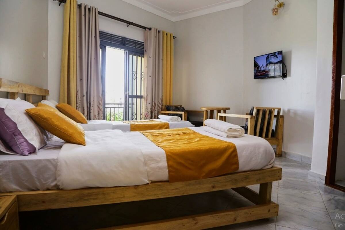 A bedroom with two beds, a TV, and a window with curtains.