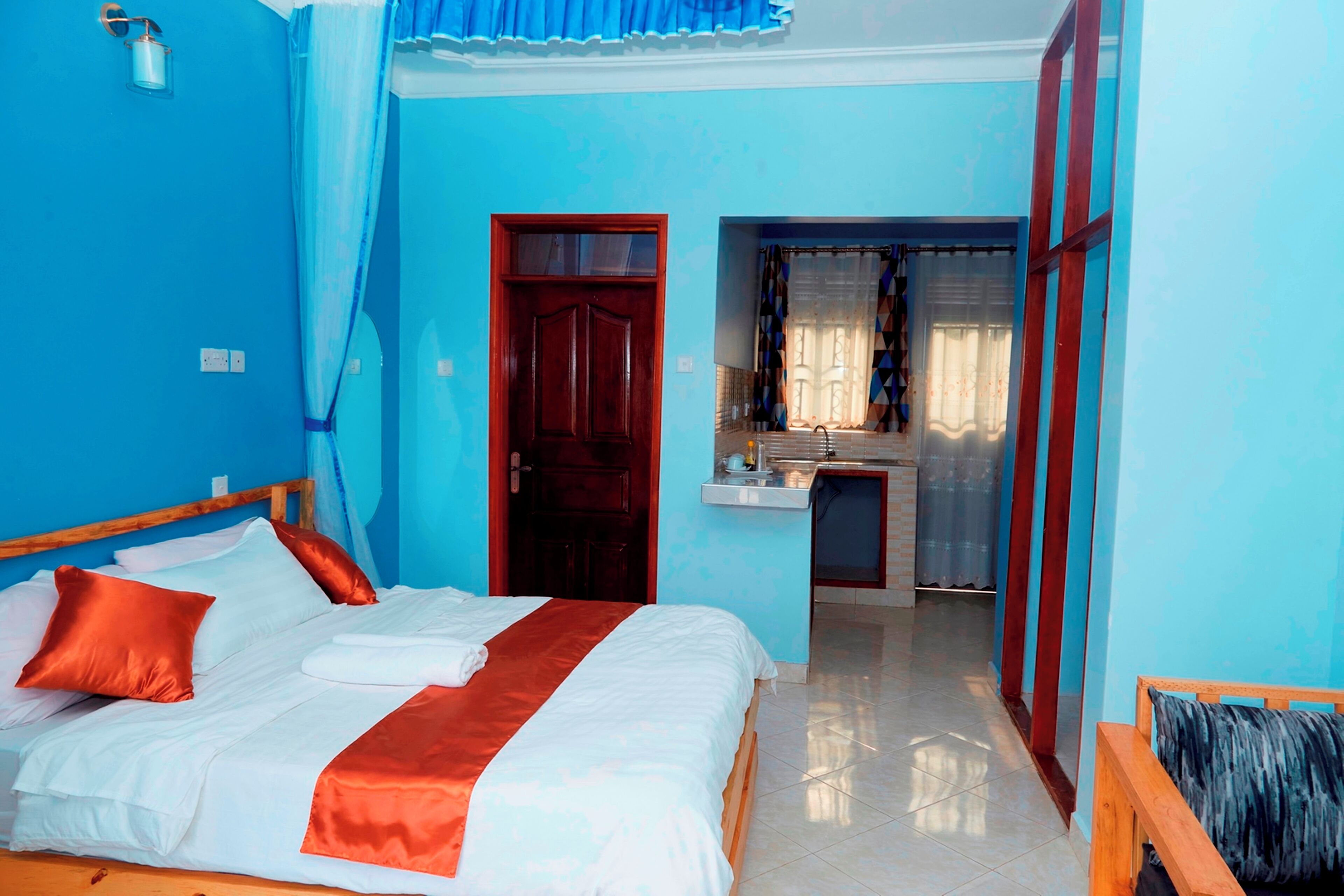 A room with a bed, a wooden bench, a small table, and a door leading to a bathroom.