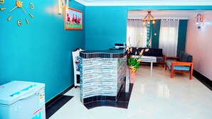 A modern living room with a blue accent wall, a black sofa, a wooden chair, and a decorative plant.