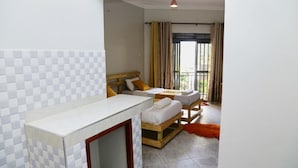A hotel room with a checkered tile wall, a wooden bed, a small round table, and a balcony with curtains.