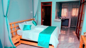 A bedroom with a wooden bed, a nightstand, a bathroom visible through an open door, and a small kitchenette area.