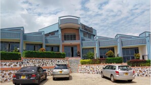 A hotel with a modern design, featuring a curved entrance and multiple balconies. There are three cars parked in front.