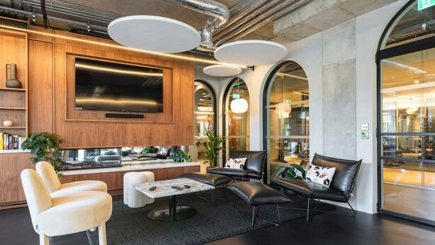 Un espace de détente moderne avec des canapés en cuir, une table basse et un téléviseur à écran plat fixé sur un panneau en bois.