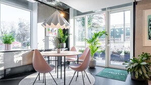 Un intérieur moderne avec une table ronde, quatre chaises, un luminaire suspendu et de grandes fenêtres ornées de plantes en pot.