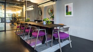 Une salle de réunion moderne, dotée d’une longue table, de chaises violettes et de grands luminaires suspendus.