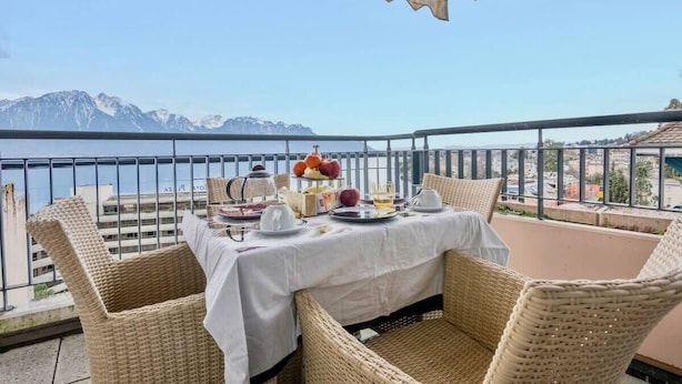 Un balcón con sillas de mimbre y una mesa preparada para una comida, con vistas a un paisaje montañoso.