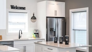 A modern kitchen with white cabinetry, a stainless steel refrigerator, a coffee maker, and a 'Welcome' sign.
