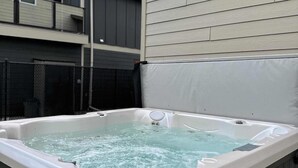 A hot tub with a wooden exterior, positioned against a house with a grey siding exterior.