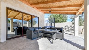 An outdoor patio with a dining table and wicker furniture, stone walls, and a view of the surrounding landscape. - Luxurious home in Prkos (Prkos)