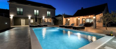A swimming pool with lounge chairs and a house in the background.