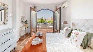 A bedroom with a bed, a desk with a chair, a small table with a plant, and a view of the outside. - La Manga Club Los Altos Townhouse 489 (Atamaría)