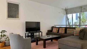 A modern living room with a flat-screen TV, a grey sofa, a coffee table, and a potted plant.