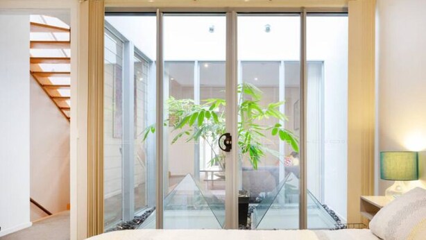 A bedroom with a large bed, a glass door leading to a balcony, and a staircase to the left.