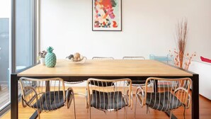 A dining area with a wooden table, metal chairs, a pineapple centerpiece, and a colorful abstract painting on the wall.