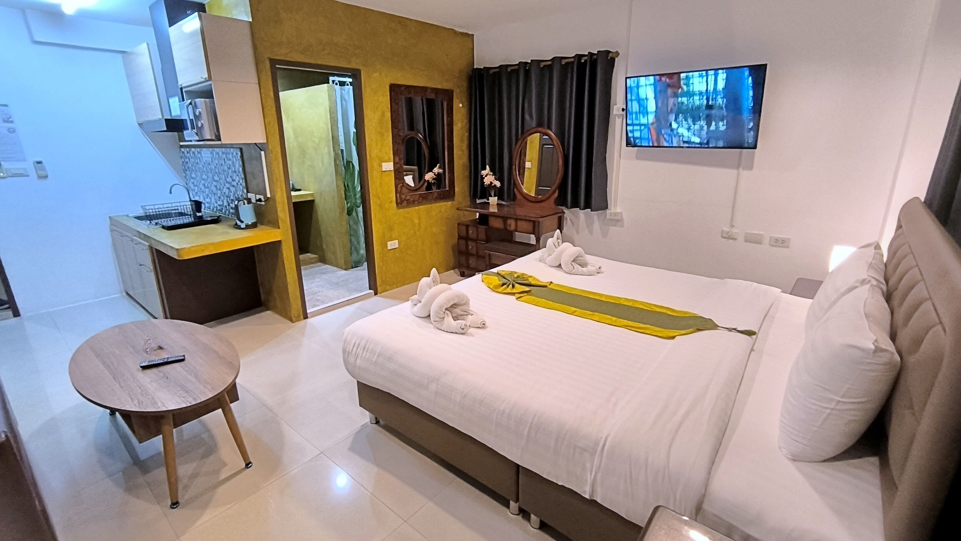 A hotel room with a bed, a small round table, a desk with a computer, a TV, and a bathroom visible through an open door.