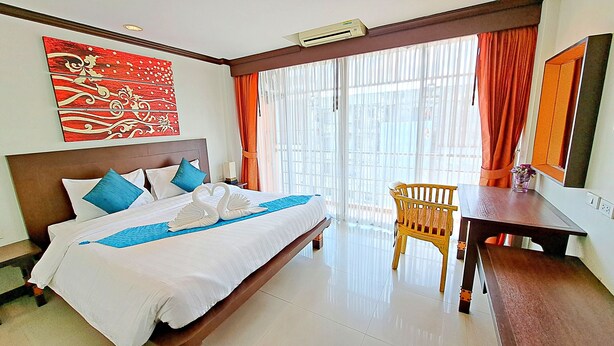A hotel room with a bed, a wooden chair, a desk, and a large window with curtains. - Southern Comfort Patong (Patong)