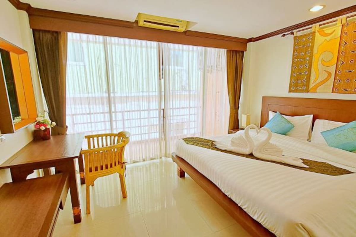 Una habitación de hotel con una cama, un escritorio, una silla y un ventanal con cortinas.