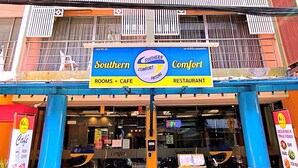 A multi-story building with balconies, a signboard for 'Southern Comfort Patong' indicating a restaurant and cafe, and a visible entrance with outdoor seating. - Southern Comfort Patong (Patong)
