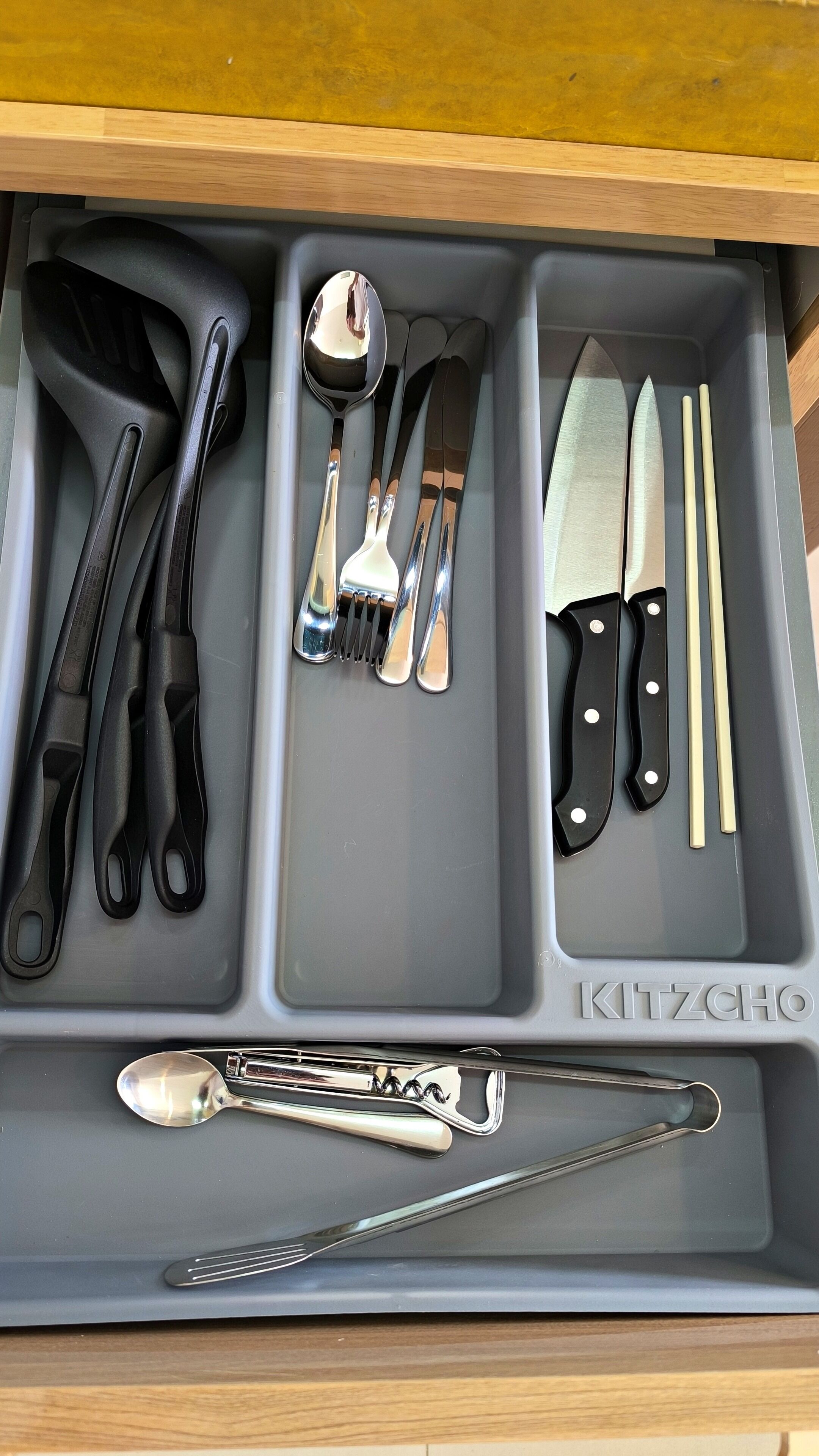 A drawer containing various kitchen utensils including tongs, spoons, forks, knives, and chopsticks.