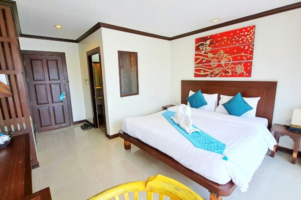 Una habitación de hotel con una cama grande, cabecera de madera, un adorno de pared rojo y una puerta de madera.