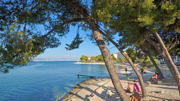 A beach with clear blue water, people relaxing on the sand, and trees providing shade. - Dani, Home-like sea View Apt, Close to Beach (Trogir)