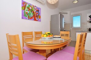 A dining area with a round glass table, wooden chairs, and purple cushions. There is a plate of fruit on the table.