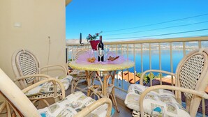 A balcony with wicker chairs and a round table, overlooking a body of water and a distant cityscape. - Dani, Home-like sea View Apt, Close to Beach (Trogir)