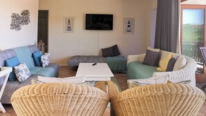 A living room with a sofa set, a TV, and wicker chairs. - Seahorse (Plettenberg Bay)